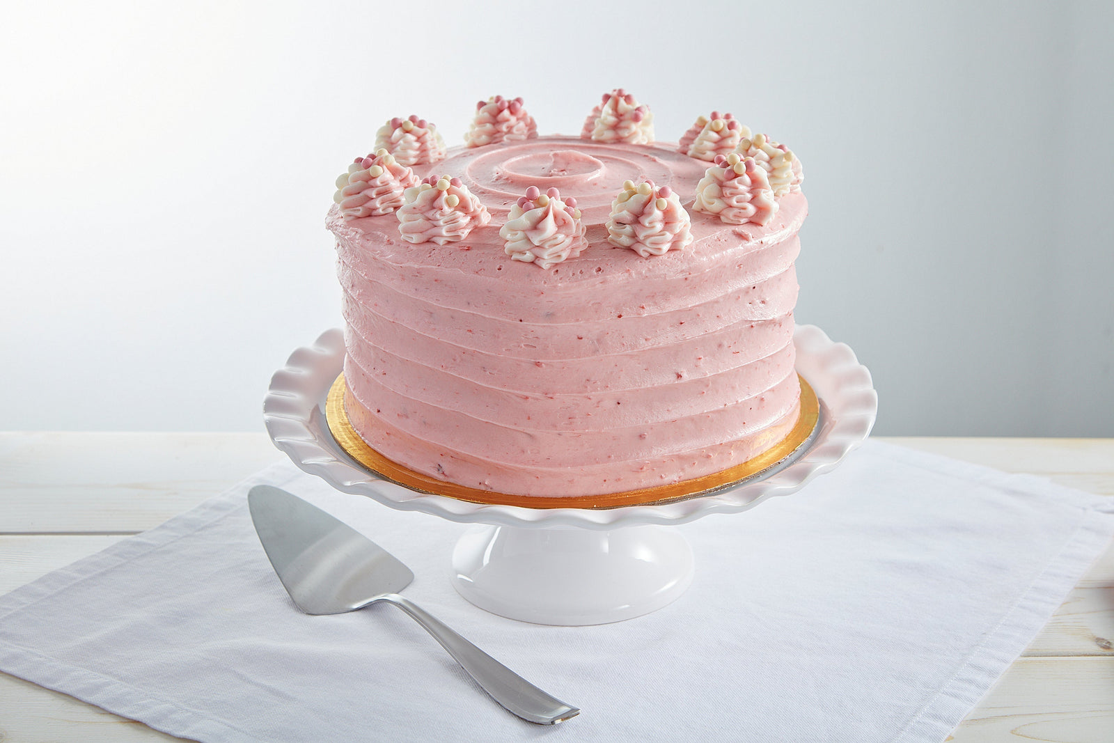 Pink strawberry frosted layer cake on a white pedestal stand