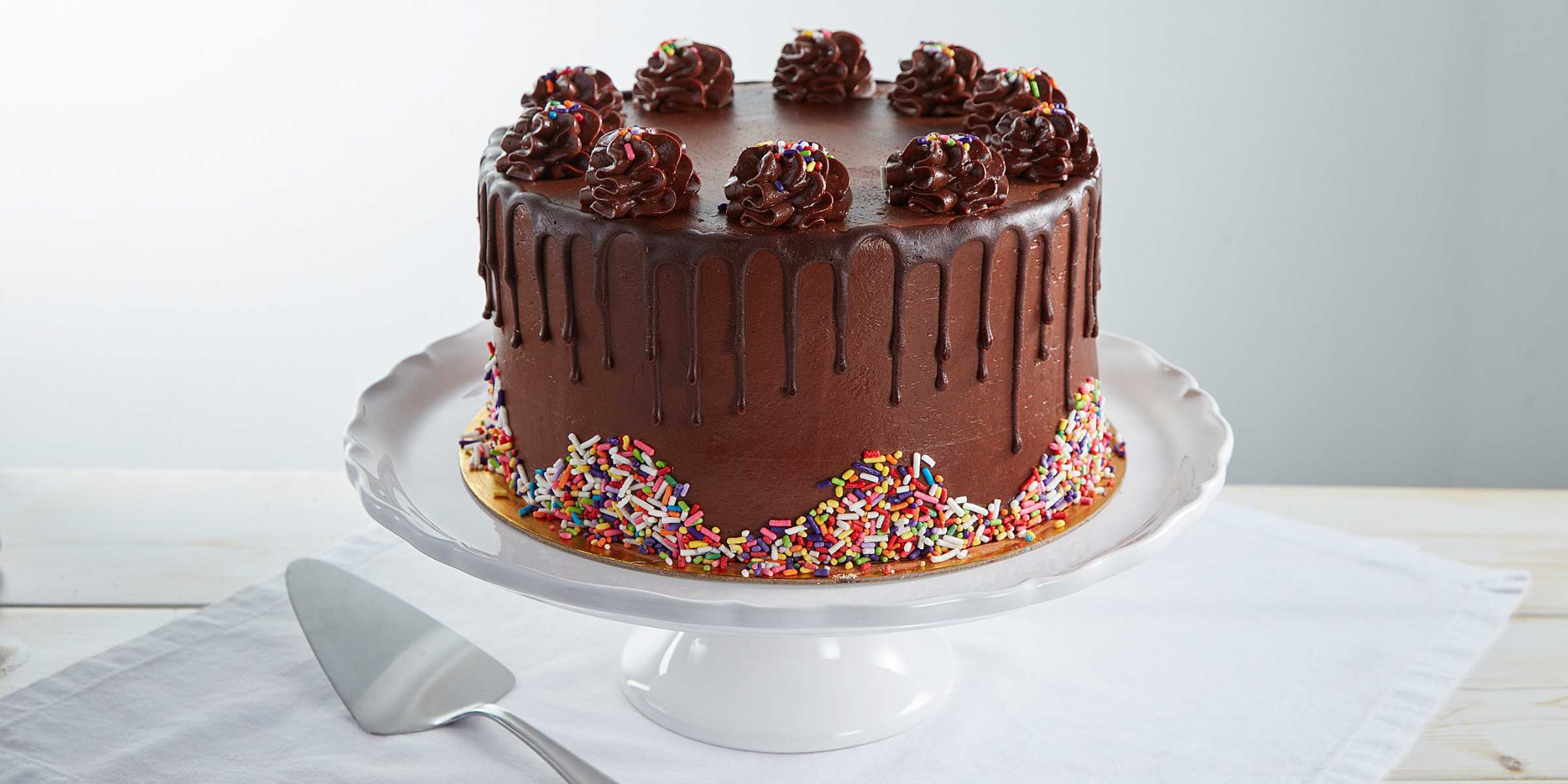 Chocolate drip cake with rainbow sprinkles on a cake stand