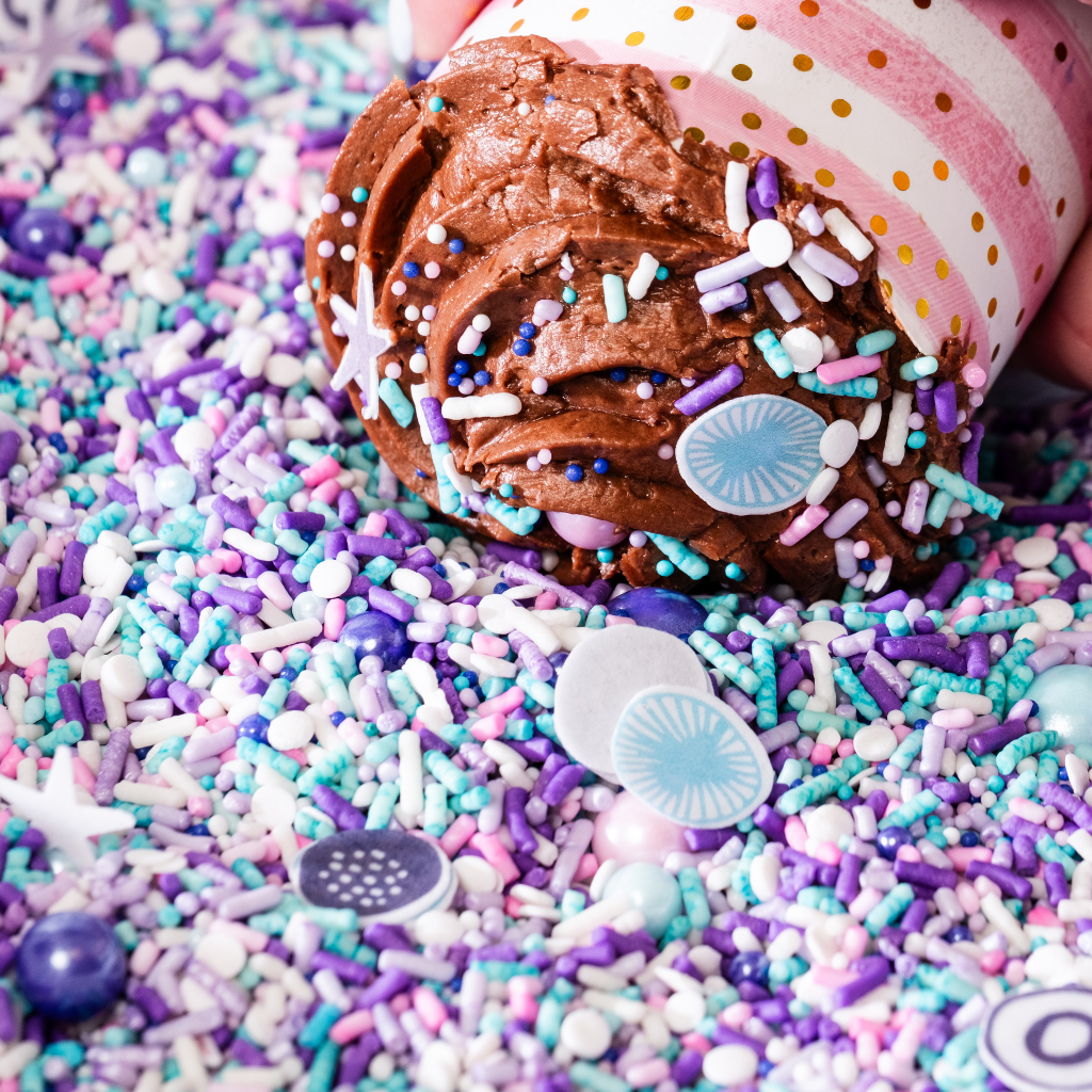 Chocolate cupcake topped with purple and blue sprinkles.