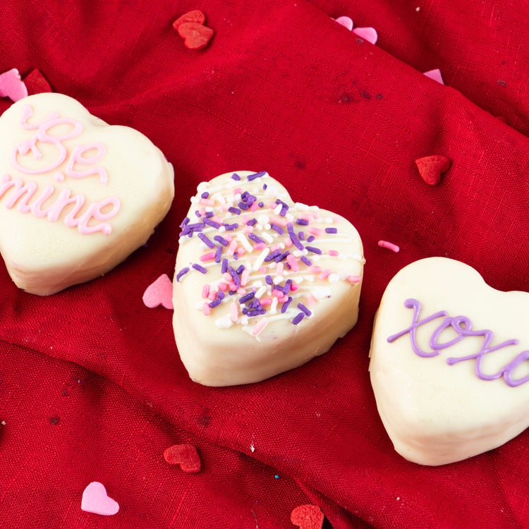 Petit Four Hearts decorated with icing on a red cloth.