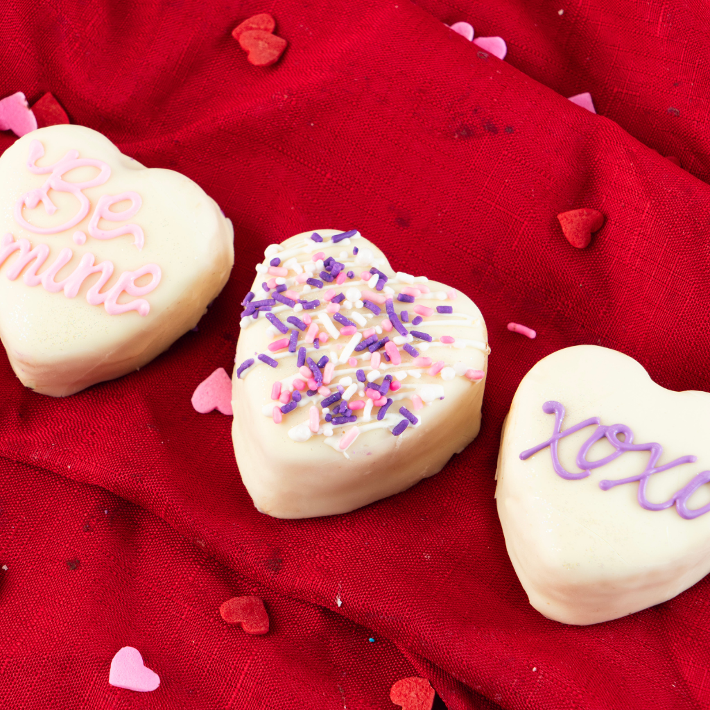 Petit Four Hearts decorated with icing on a red cloth.