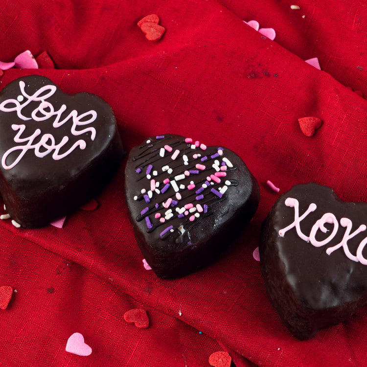 Three chocolate heart petit fours on a red fabric background.
