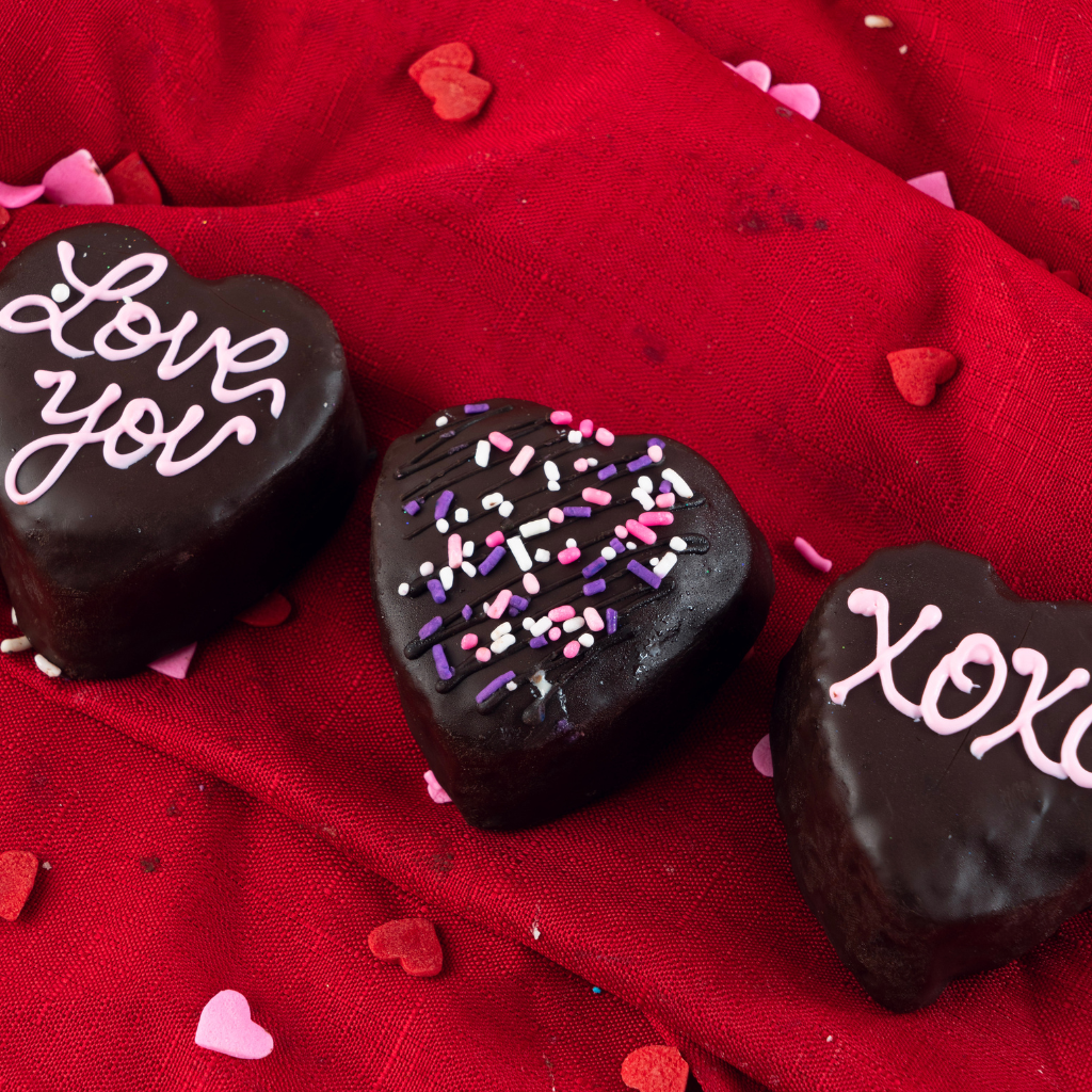 Three chocolate heart petit fours on a red fabric background.