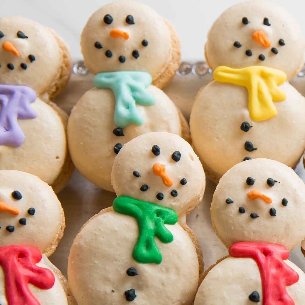 Snowman macarons with colorful icing scarves on a tray.