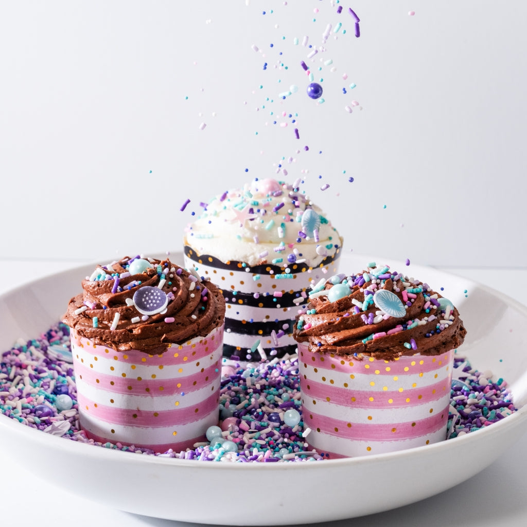 Assorted cupcakes with sprinkles in a white bowl.
