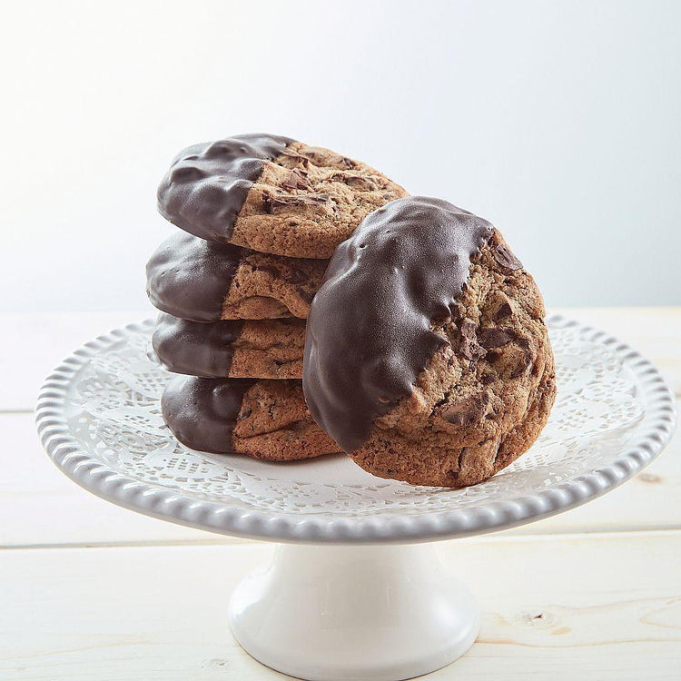 Chocolate-dipped chocolate chunk cookies on a white cake stand.