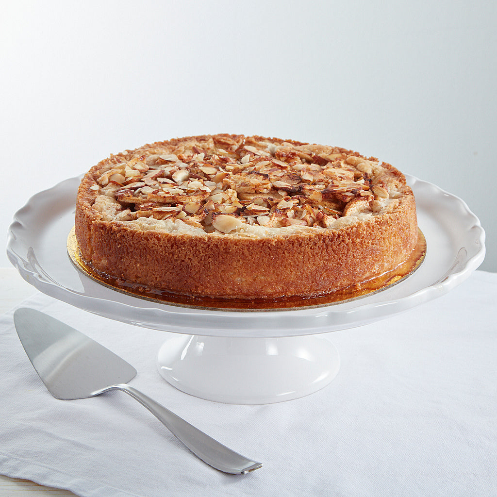 Deep dish apple tart topped with almonds on a white cake stand.
