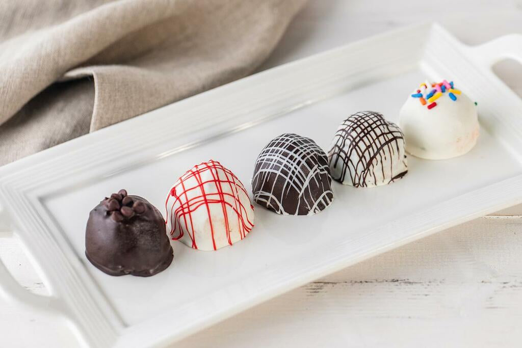 Five chocolate chip cake balls on a white rectangular platter.