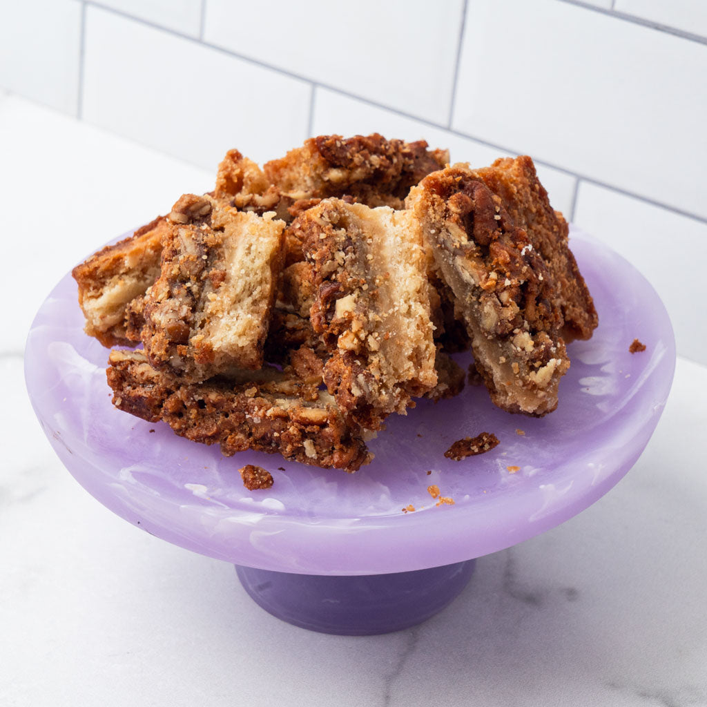 Edges pecan pie bars on a purple pedestal stand.
