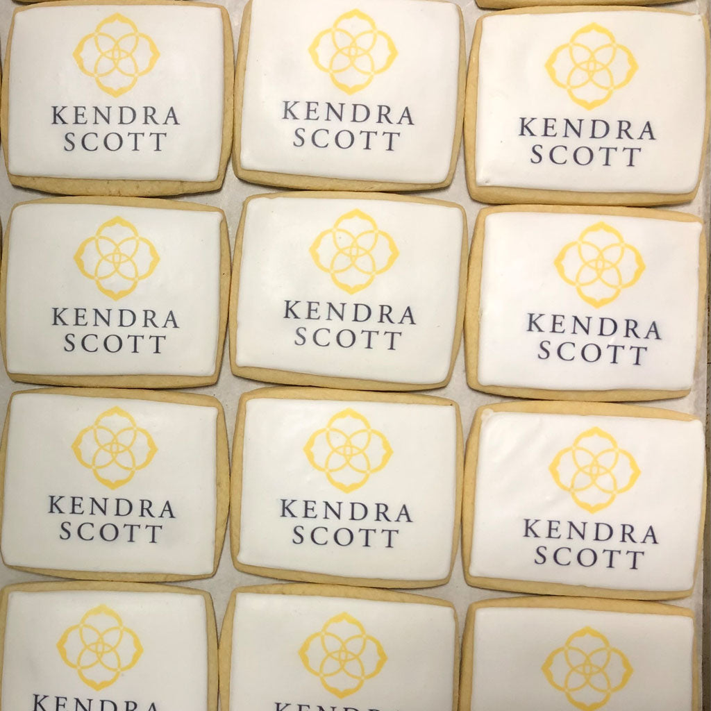 Square cookies with white icing and yellow Kendra Scott logos.
