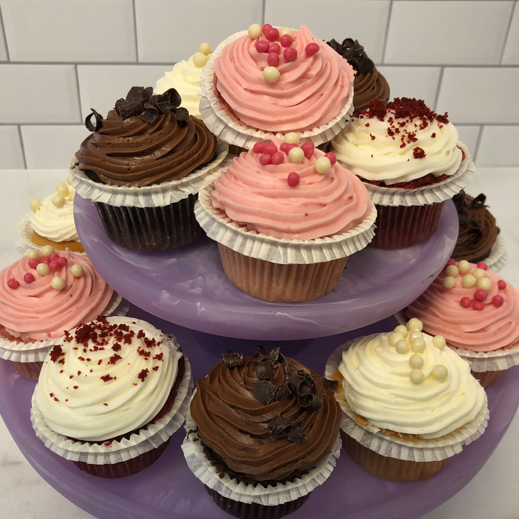 Mini red velvet cupcakes with assorted frosting on a purple stand.