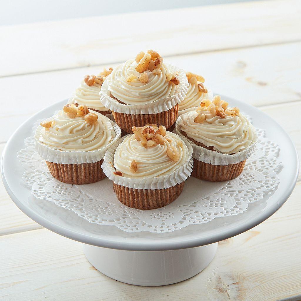 Five walnut-topped cupcakes with white frosting on a stand
