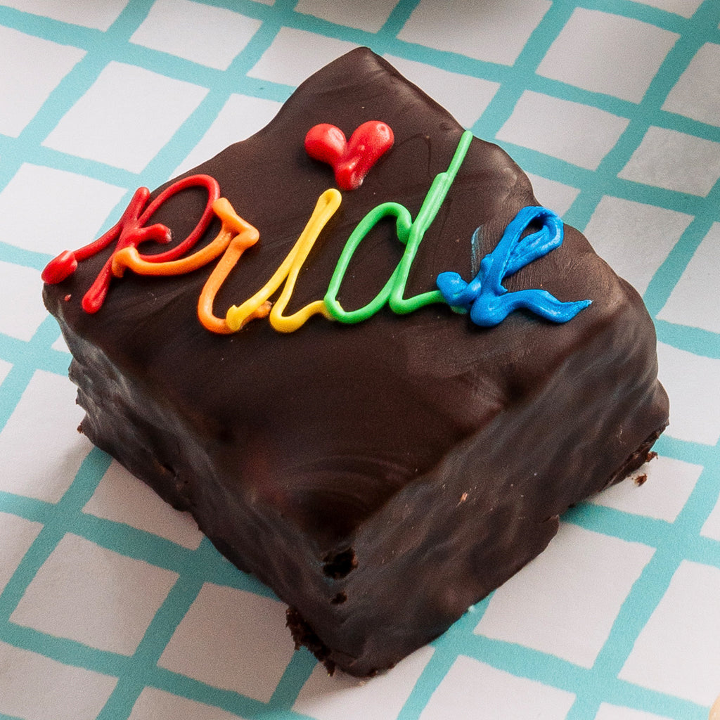 Pride Petit Four with rainbow icing on a blue grid background.