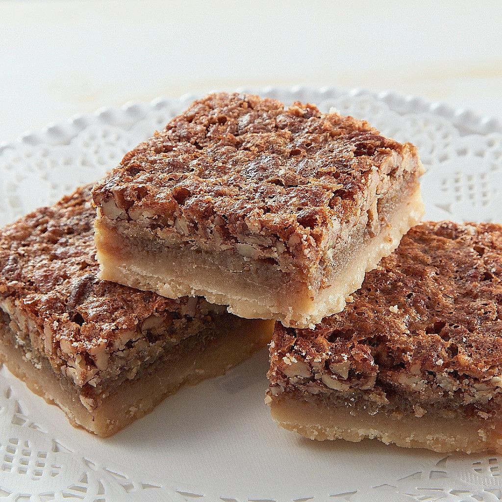 Three square pecan pie bars stacked on a white lace doily.
