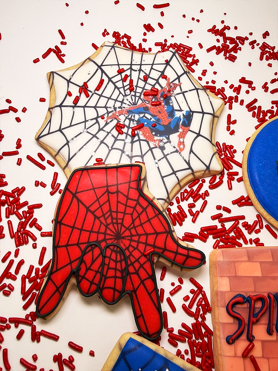 Spiderman cookies with red and blue icing on a sprinkle background.