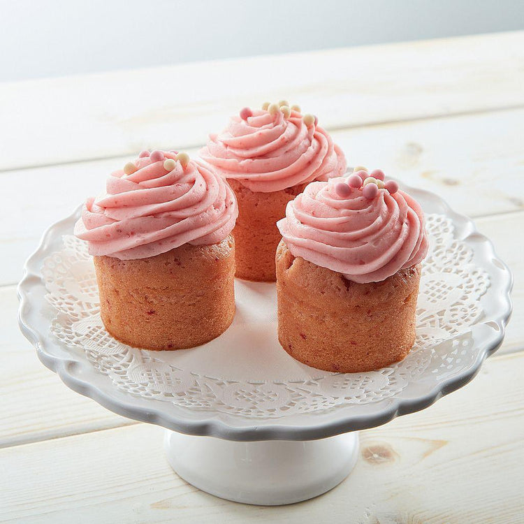 Three strawberry cupcakes with pink frosting on a white stand.