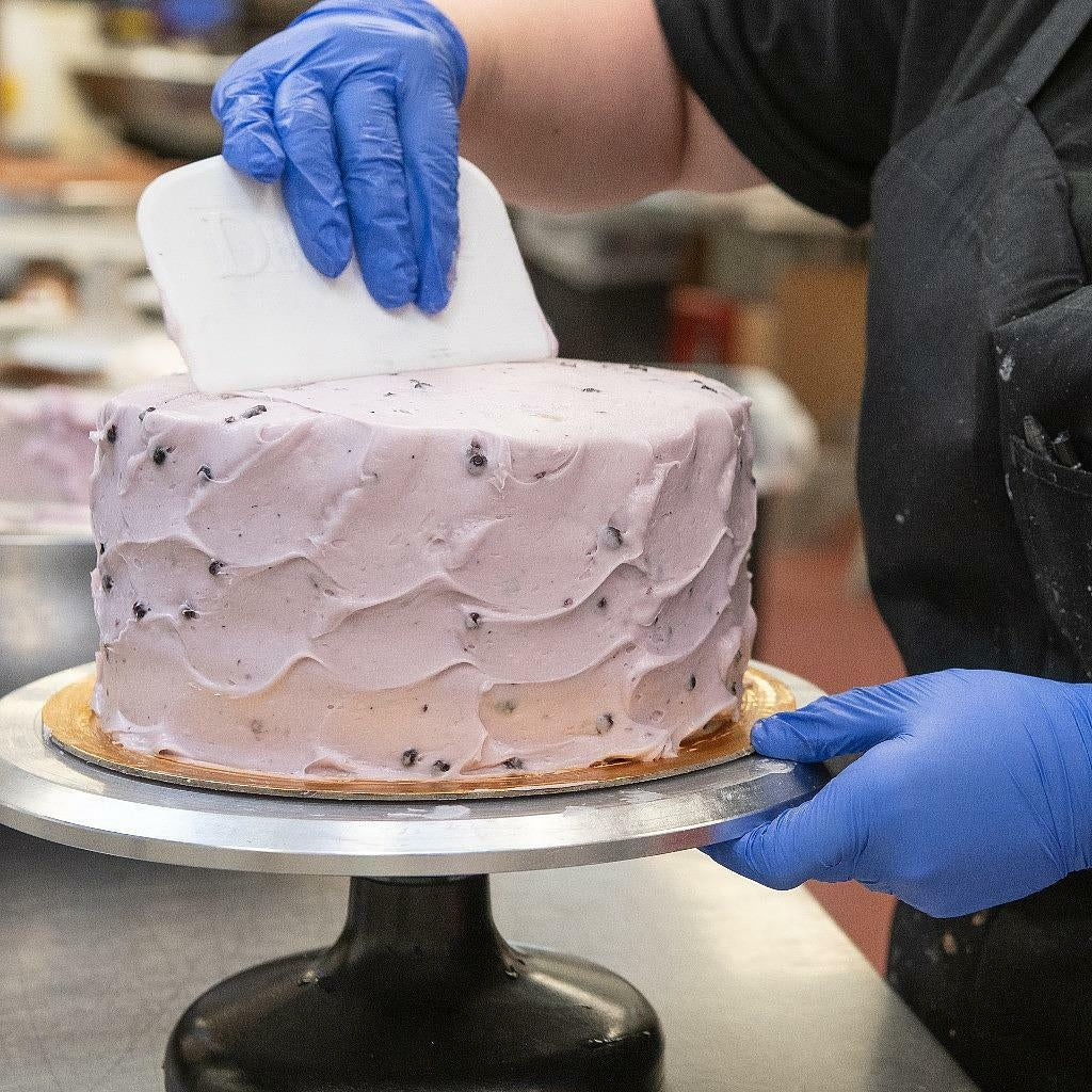 Baker smoothing lavender frosting on a round berry cake