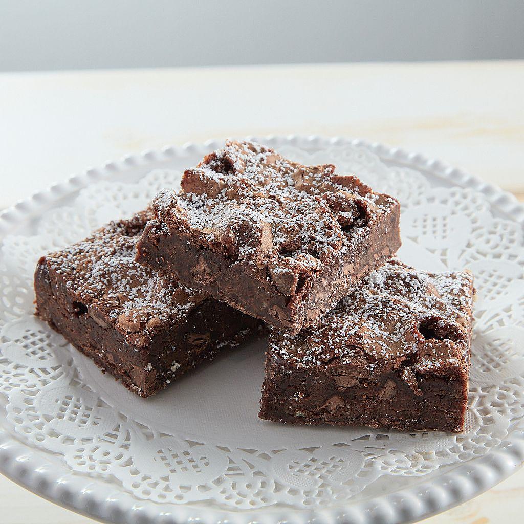 Three chocolate brownies dusted with sugar on a lace doily.