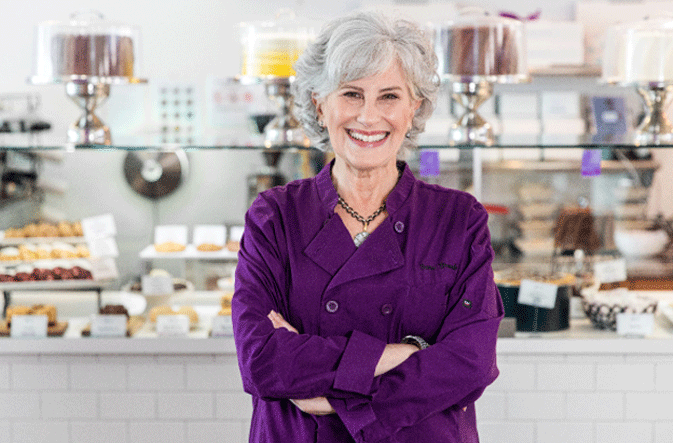 Smiling woman in a purple chef coat standing in a bakery.