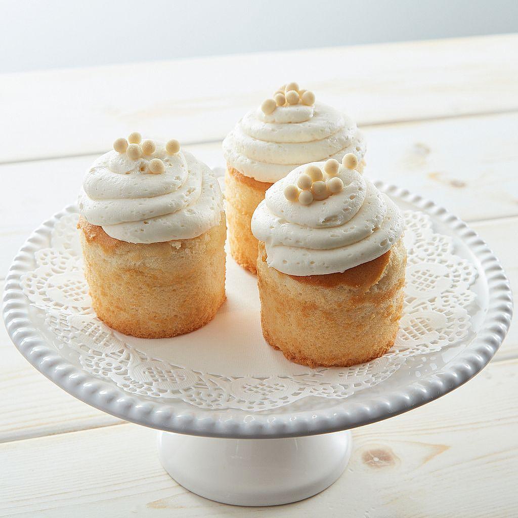 Three vanilla cupcakes with white frosting on a cake stand.
