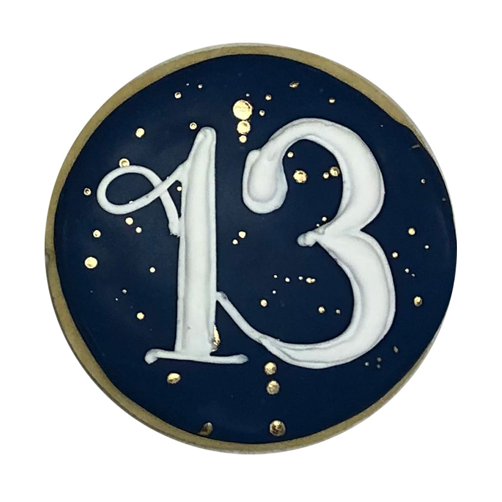 Round 13th age plaque with navy icing and gold accents.