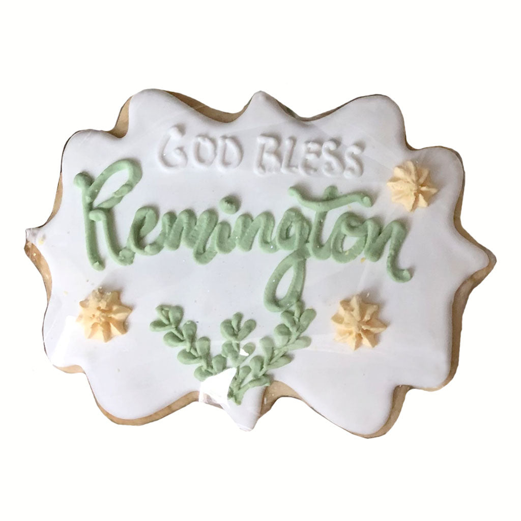 Baptism plaque cookie with green name and floral icing details.