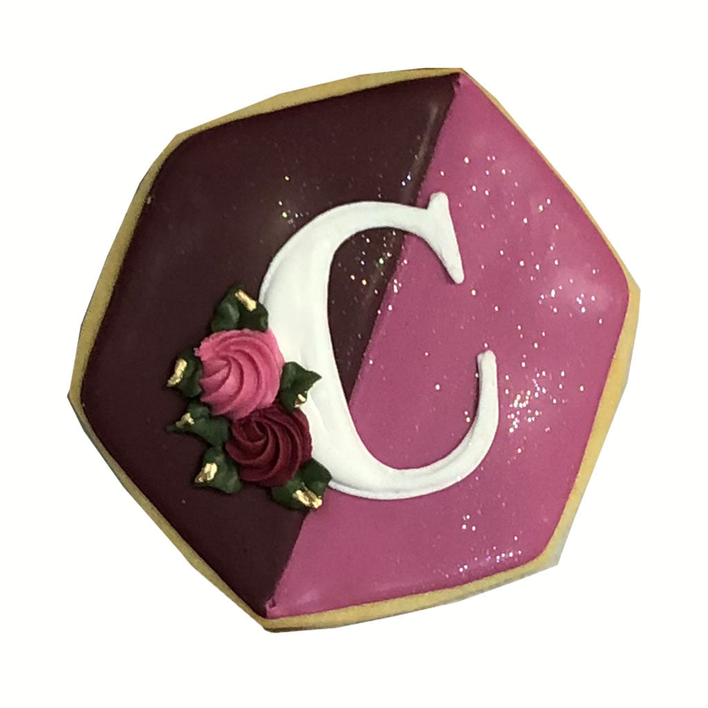 Hexagon initial plaque with letter C, pink and maroon icing.