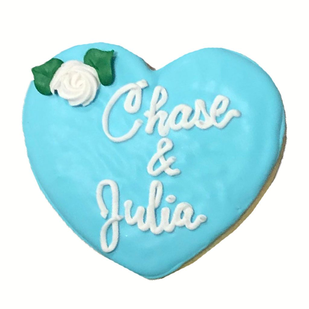 Blue heart-shaped cookie with white icing names and a rose.
