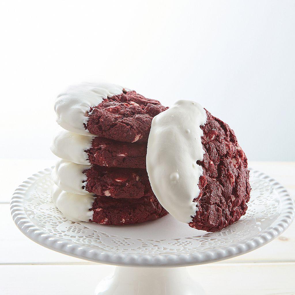 White-dipped red velvet cookies stacked on a white cake stand.
