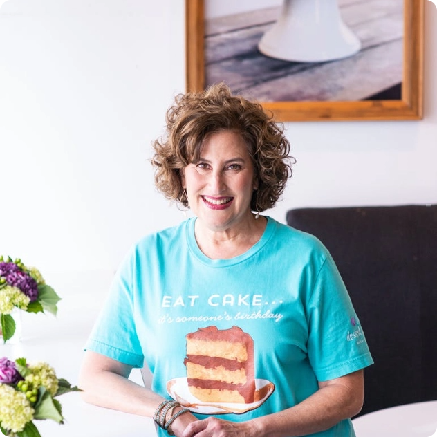 Woman wearing a teal Eat Cake t-shirt smiling at a table